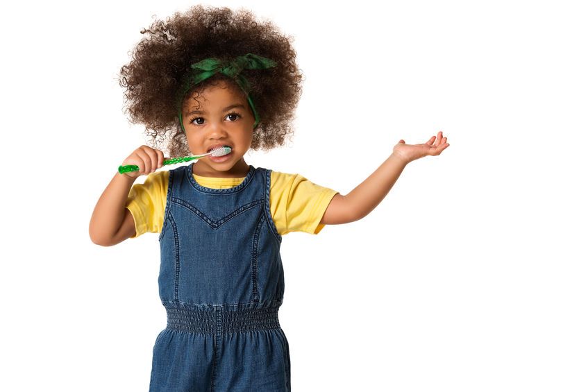 Young child with afro and overalls using green toothbrush